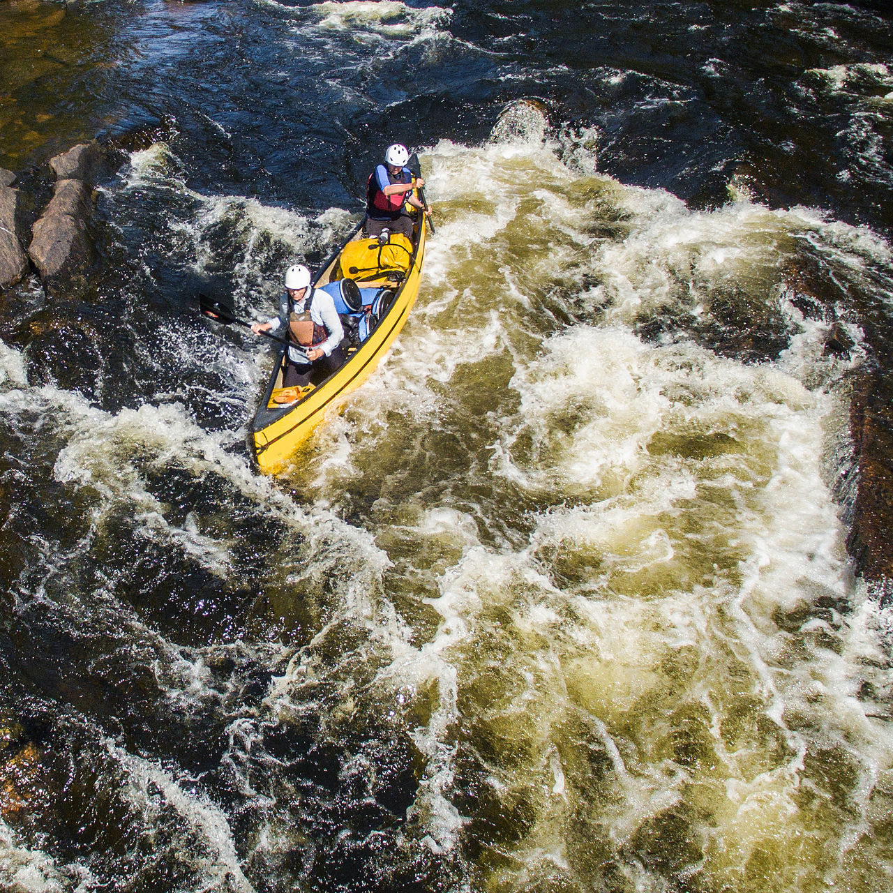A group of people paddling in whitewater with a canoe